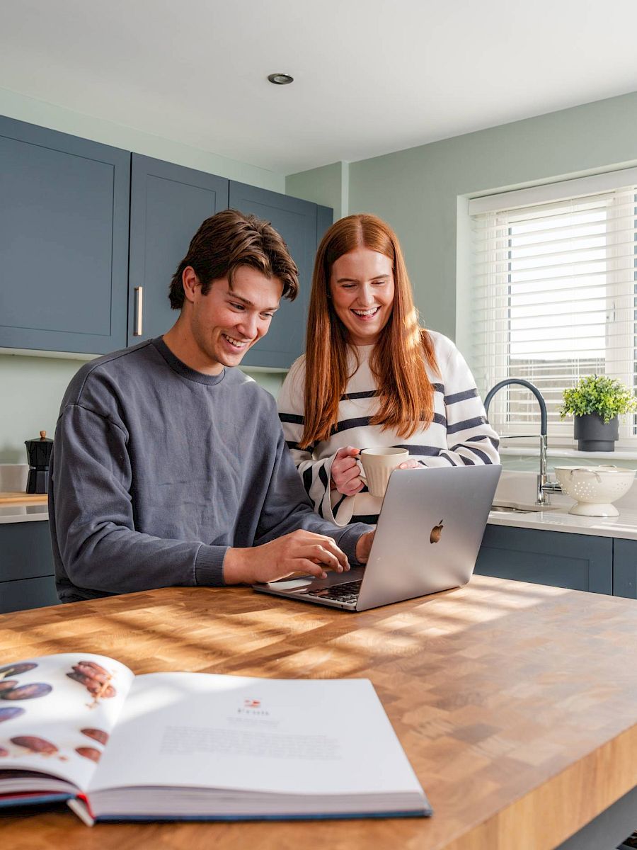 Happy couple in kitchen looking at laptop