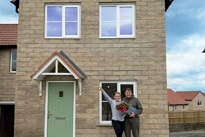 Young couple stood smiling outside their new home