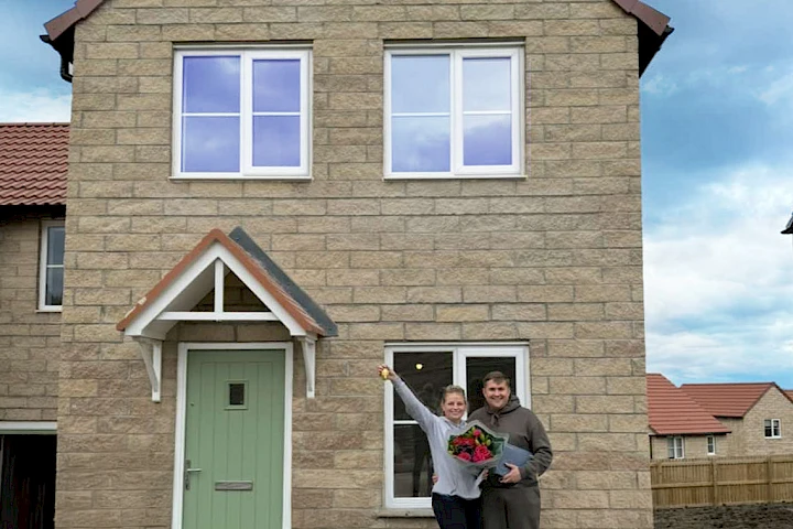 Young couple stood smiling outside their new home