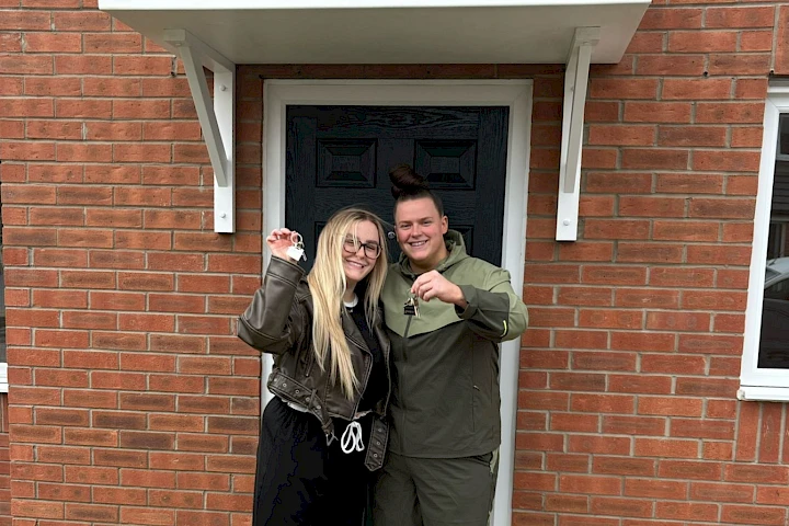 Young couple holding keys outside front door of new home, smiling