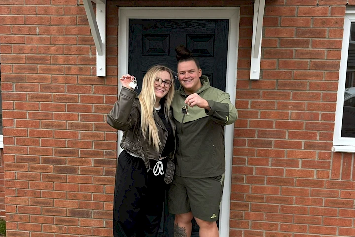 Young couple holding keys outside front door of new home, smiling