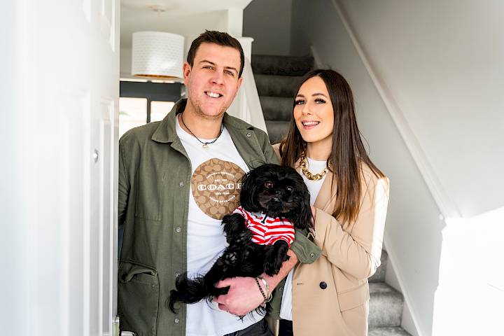 Happy couple stood with dog in doorway.