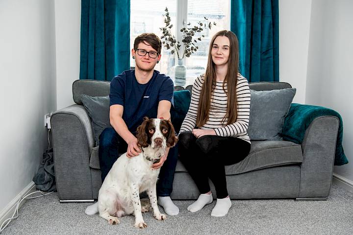 Happy couple sat with dog in new lounge.